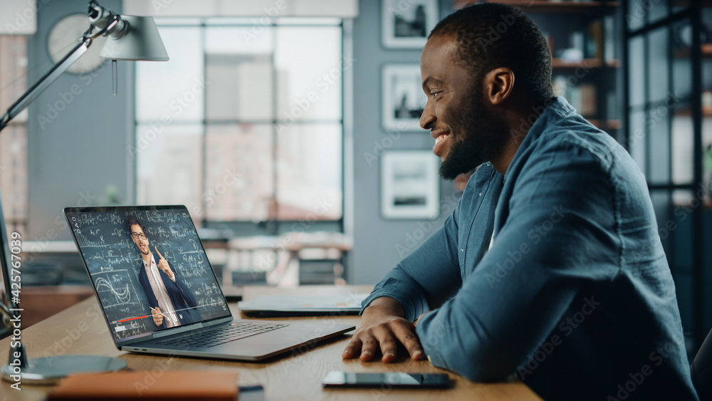 Poster african american man having an online video lesson on laptop computer while sitting behind desk in l