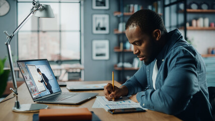 African American Man Having an Online Video Lesson on Laptop Computer while Sitting Behind Desk in Living Room. Freelancer Working on His Skills or Student Doing Homework Over the Internet.