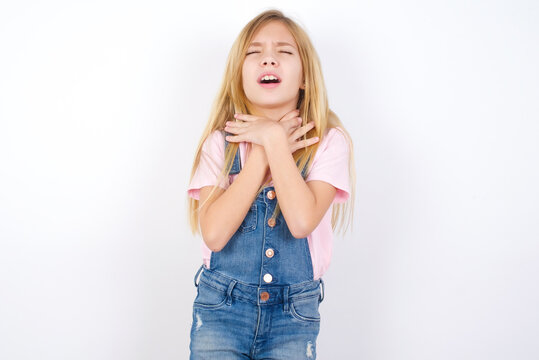 beautiful caucasian little girl wearing denim jeans overall over white background shouting suffocate because painful strangle. Health problem. Asphyxiate and suicide concept.