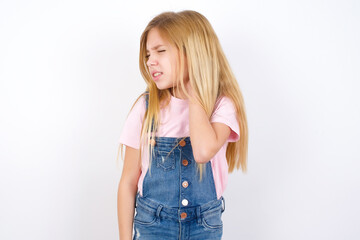 Fototapeta premium beautiful caucasian little girl wearing denim jeans overall over white background Suffering of neck ache injury, touching neck with hand, muscular pain