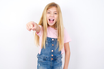 beautiful caucasian little girl wearing denim jeans overall over white background pointing displeased and frustrated to the camera, angry and furious ready to fight with you.