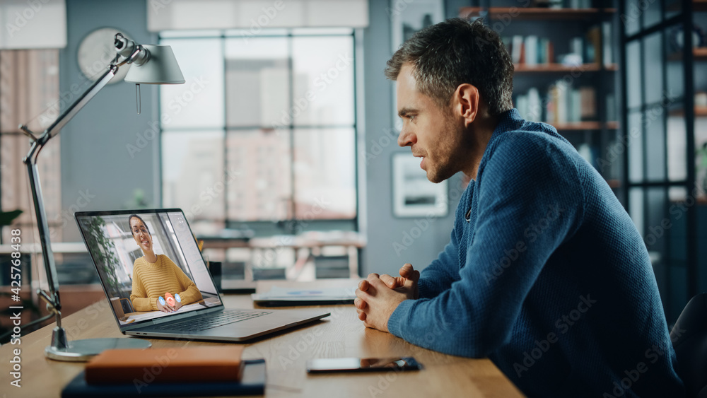 Aufkleber Handsome Caucasian Man Having a Video Call on Laptop Computer while Sitting Behind Desk in Living Room. Freelancer Working From Home and Talking to Colleagues and Clients Over the Internet.