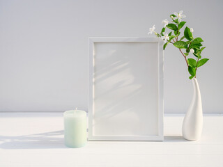 Mock up poster frame Gardenia flower in modern white vase  and green candle  on white wood  table and cement wall background with long shadow