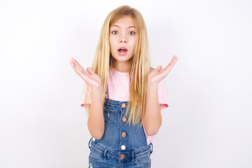 Surprised terrified beautiful caucasian little girl wearing denim jeans overall  gestures with...