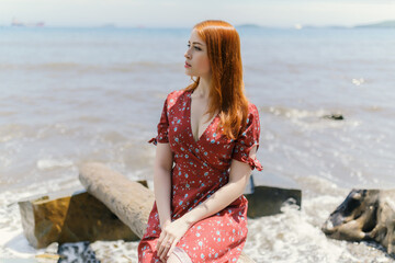 Young redhead woman in white dress enjoys sea.