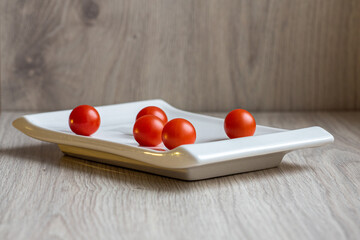 cherry tomatoes lie on an abela rectangular plate on a wooden light background