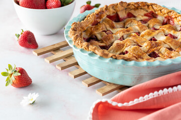Close up of a homemade lattice topped strawberry and rhubarb pie cooling on a wooden trivet.