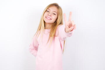Fototapeta premium Beautiful caucasian blonde little girl wearing pink sweater directs fingers at camera selects someone. I recommend you. Best choice