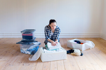 A young woman puts away seasonal clothes and items for storage in boxes. Spring cleaning