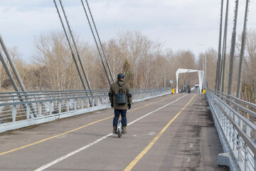 A man rides an electric mono wheel. View from the back. A road for scooters and pedestrians. Cold season. © Sergei Tim
