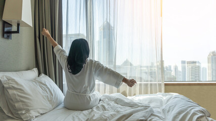 Hotel Relaxation with Asian woman waking up from good sleep in weekend morning resting in comfort...