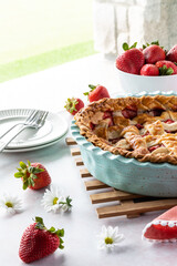 A strawberry rhubarb pie on a wooden trivet next to a bright window, ready for serving.