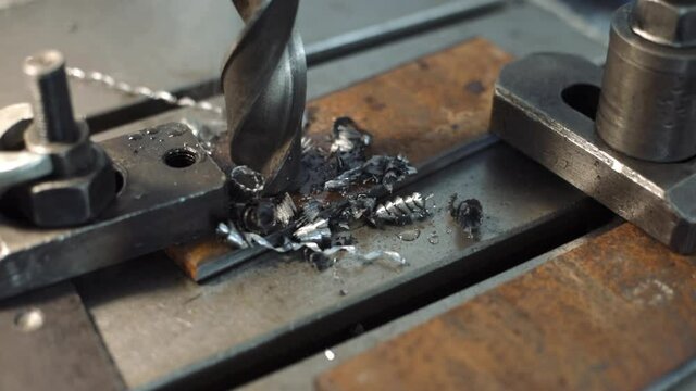 A large diameter drill bit drills a metal plate and metal chips are formed. Working in a lathe shop. Top view.