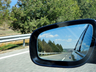 Landscape and road reflection in car rearview black mirror.