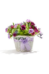 Subject shot of dark and light violet roses in white basket decorated with silk ribbon. Fine faux flowers for interior design are isolated on the white background. 