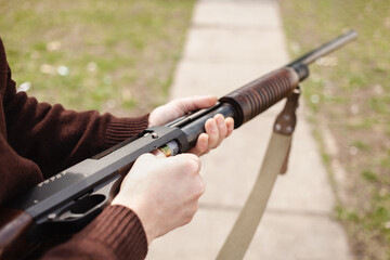 A man charges a pump-action shotgun with a Ammo. 12 caliber. Tyre outdoor. A man in headphones and goggles is preparing to shoot. Firearms for sports shooting, hobby. copy space