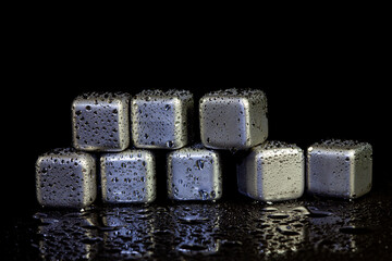 Stainless steel cubes simulating ice for cooling drinks on a black surface with a reflection.