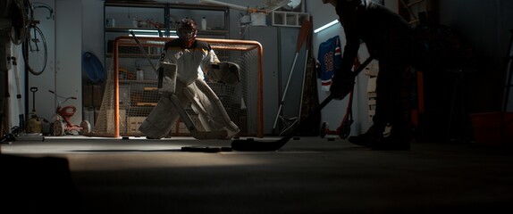 Kid boys friends or brothers practicing hockey shots inside a covered garage. Shot with 2x...