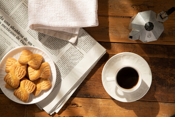 Breakfast composition: white coffee cup with italian espresso, grey coffee maker, biscuits, newspaper and white cloth.