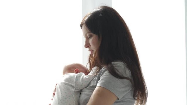 Happy mother holding her baby while standing by the window. High quality 4k footage