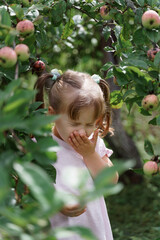 caucasian child girl sneezes among the branches of an apple tree with fruits.
