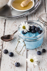 Close up of blue spirulina yogurt parfait topped with blueberries with honey in behind.