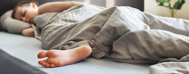 boy sleep sweetly in the bed in the morning. child lies on pillow under blanket. banner