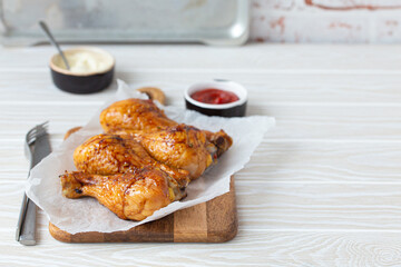 Roasted golden chicken legs drumsticks on baking paper on wooden board served with ketchup and...