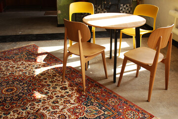 Fancy dinning room interior. Wooden and plastic yellow chairs by the round table, colorfull carpet on the floor. Loft desighn
