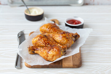Roasted golden chicken legs drumsticks on baking paper on wooden board served with ketchup and...