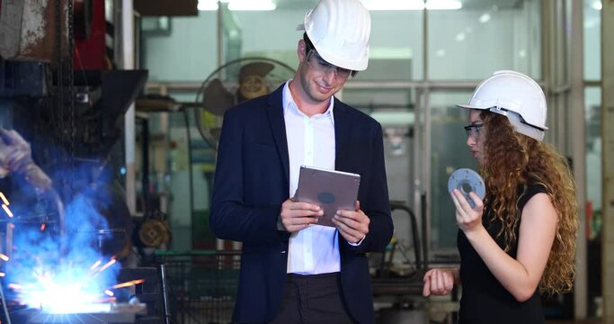 Manufacturing Factory female Mechanical Engineering programer Works on Personal Computer and man worker are working with Robotic Arm at industrial factory