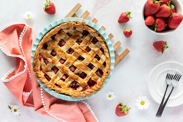 Top down view of a lattice topped strawberry rhubarb pie fresh out of the oven, cooling on a wooden trivet.