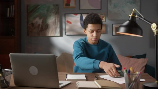 Black African boy student writing notes in copybook and using phone, doing homework on video conference call. Remote home video lesson. Home isolation, coronavirus quarantine. 