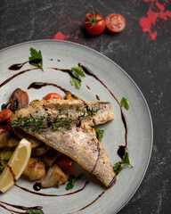 Dietary fish dish, hearty and healthy lunch. Fried river fish with vegetables. Plate of cooked Fish on black background. Close up, High angle view. 