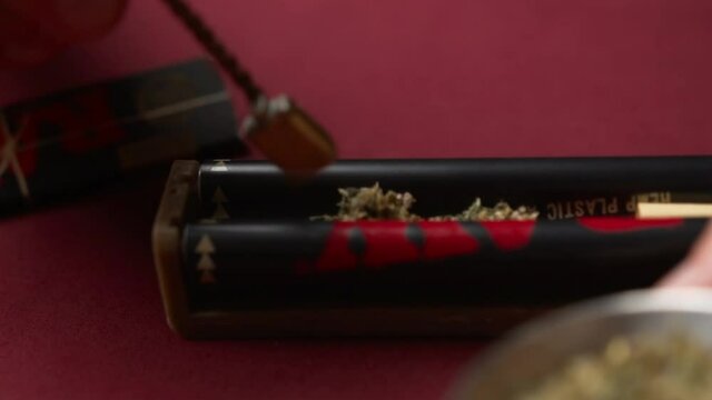 The man took from a grinder in a measuring spoon of the crushed dry weed of marijuana and puts it in the machine for rolling of cigarettes. Preparing to twist the joint with cannabis