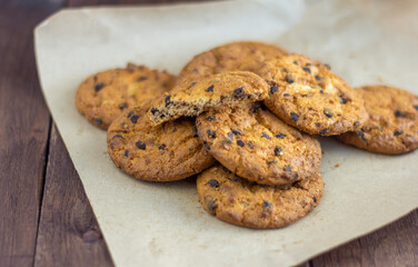 Delicious oatmeal cookies with chocolate pieces in wrapping paper on a wooden background.