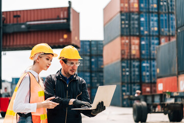 workers teamwork man and woman in safety jumpsuit workwear with yellow helmet use laptop and talking at cargo container shipping warehouse. transportation import,export logistic industrial service