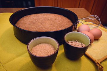 Whisk and baking pan with homemade traditional hazelnut cake from Piedmont (Italy) and raw ingredients: cane sugar, eggs and flour of nocciola piemonte (the typical hazelnut variety of Piedmont)