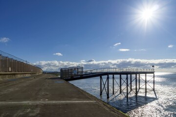 Fototapeta na wymiar A walkway on the shore with a backlit jetty.