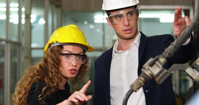 Manufacturing Factory female Mechanical Engineering programer Works on Personal Computer and man worker are working with Robotic Arm at industrial factory