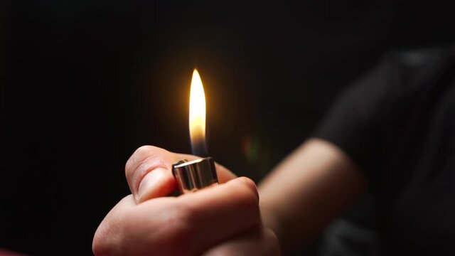 A white man lights a lighter with his hands and it burns brightly. Flame close up