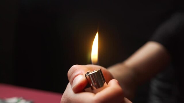 The man lit a lighter and sparks formed and smoke went up and a bright fire burned. In a dark room