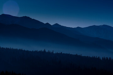 Tatra Mountains and the hills at night. The valleys are hidden in the fog, silhuettes of the trees can be seen from the shadows. Selective focus on the ridge, blurred background.