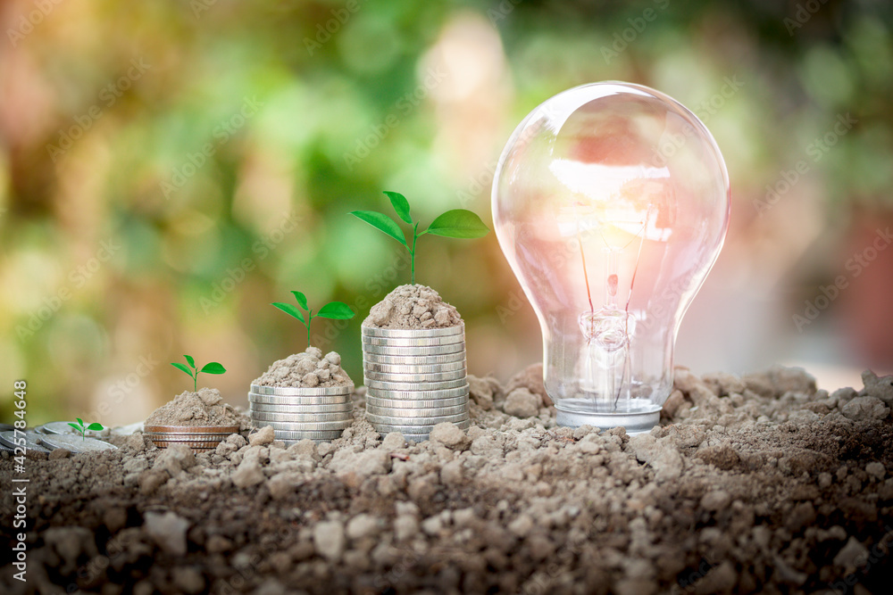 Poster energy saving light bulb and coin stacks with soil on top and tree are growing to show concept savin