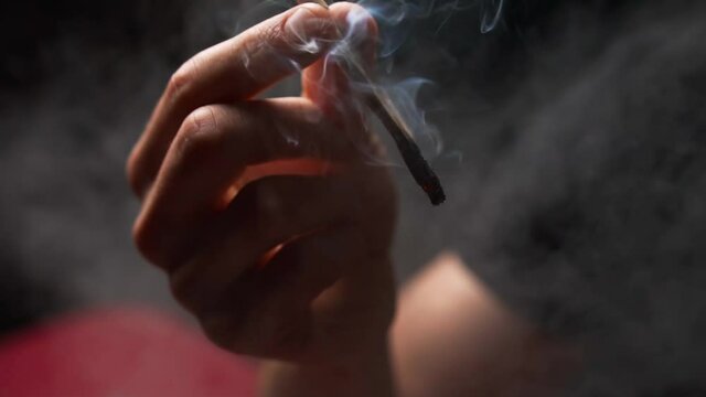The man is addicted to weed drugs and smokes a twisted joint of cannabis. Smoke comes from a cigarette. Unconventional marijuana treatment.