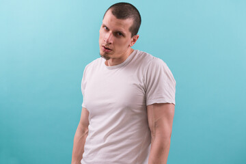 Angry caucasian man in white t-shirt dangerously and suspiciously looks at the camera on the light blue background. Serious. Seriously. Sideways glance. Annoyed. Unhappy