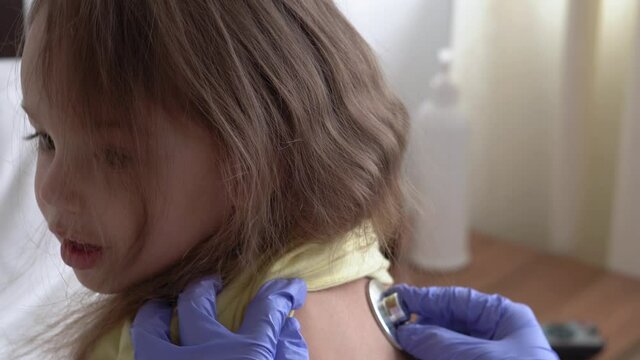 authentic cute caucasian cute young woman nurse or doctor pediatrician examine with statoscope minor preschool baby girl kid on white bed in hospital. medicine and health, pediatrics, covid-19 concept