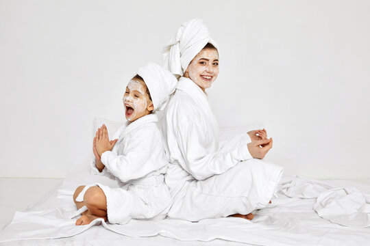 mother and daughter are sitting with towels on head and facial mask.