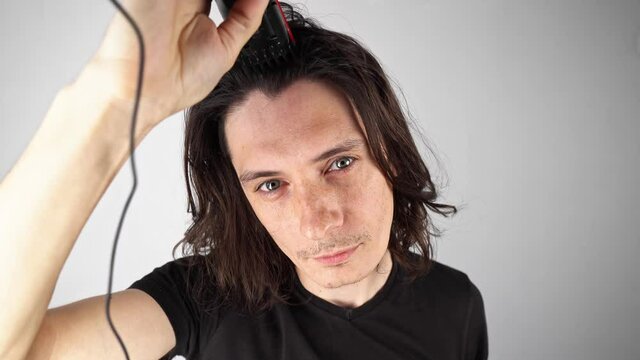 Man cuts his long hair on his head with a clipper in front of the camera. A radically new change in style and appearance
