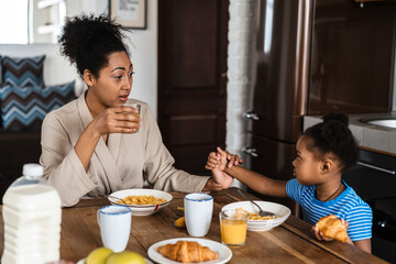 Black mother and daughter holding hands together while having breakfast